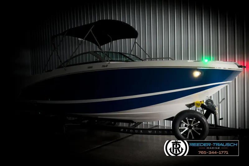 Slide: The Image of 2025 Four Winns HD3 boat with blue hull and trailer in a dimly lit showroom. - 4