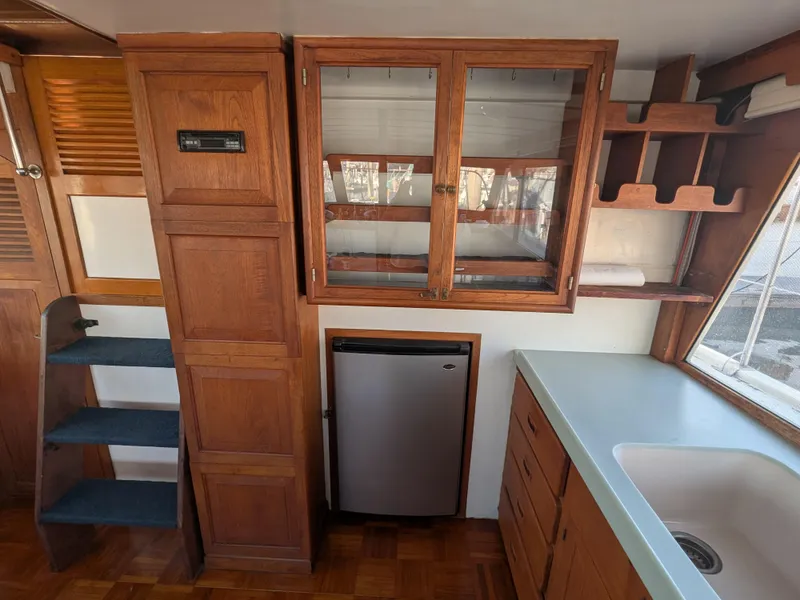 Slide: The Image of 1985 Roughwater 41 Pilothouse interior with wooden cabinetry, compact fridge, and sink. - 11