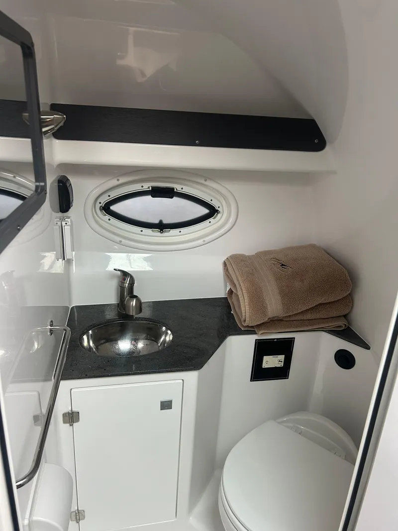 Slide: The Image of 2022 Monterey 295 Sport Yacht bathroom with sink, toilet, and porthole window. - 19