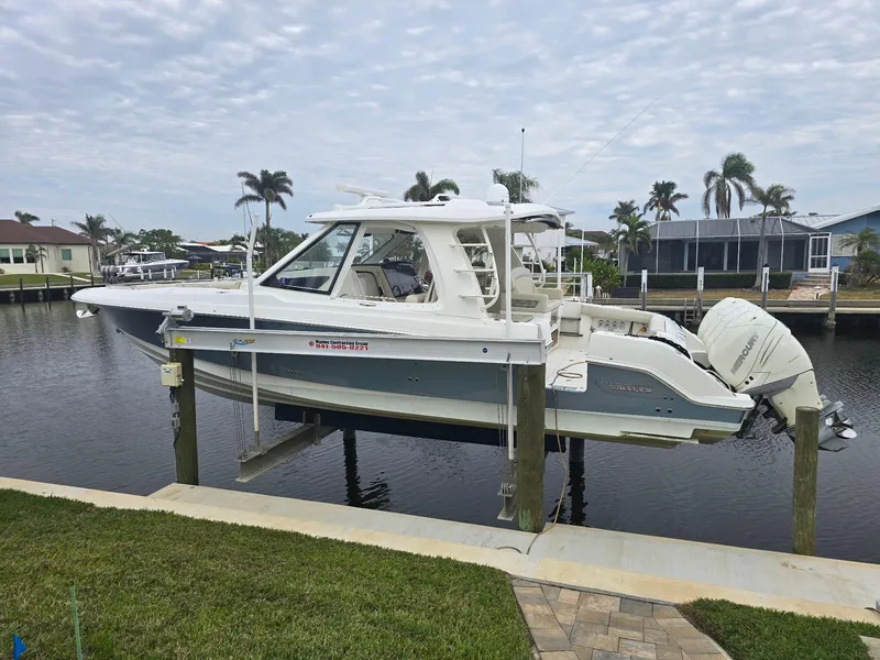 Slide: The Image of 2019 Boston Whaler 380 Realm boat docked by waterfront homes, palm trees in background. - 2