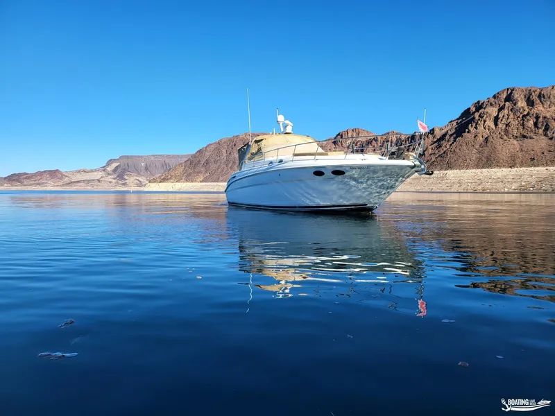 Slide: The Image of 2003 Sea Ray 380 Sundancer yacht on calm water with rocky shoreline backdrop. - 2