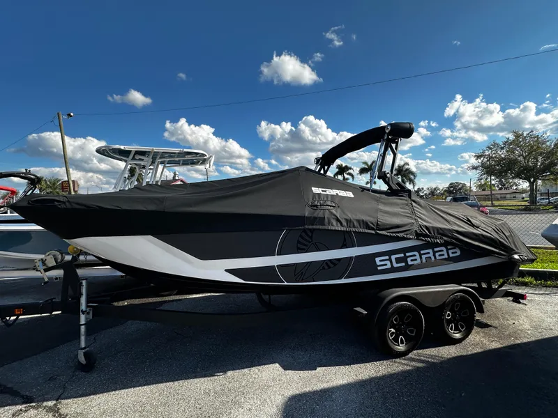 Slide: The Image of 2024 Scarab 235 Wake ID boat with cover, parked on trailer under blue sky. - 2