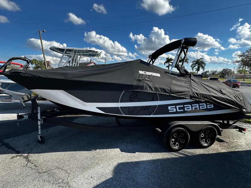 Slide: The Image of 2024 Scarab 235 Wake ID boat covered, parked on trailer under blue sky. - 6