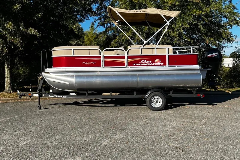 Slide: The Image of 2025 Sun Tracker Party Barge 18 DLX pontoon boat on trailer, parked outdoors. - 2