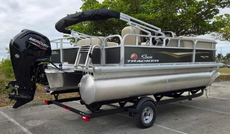 Slide: The Image of 2025 Sun Tracker Party Barge 18 DLX pontoon boat on trailer, parked outdoors. - 12