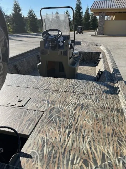 Slide: The Image of 2025 Tracker Grizzly 1860 CC boat with camo design, parked outdoors. - 2