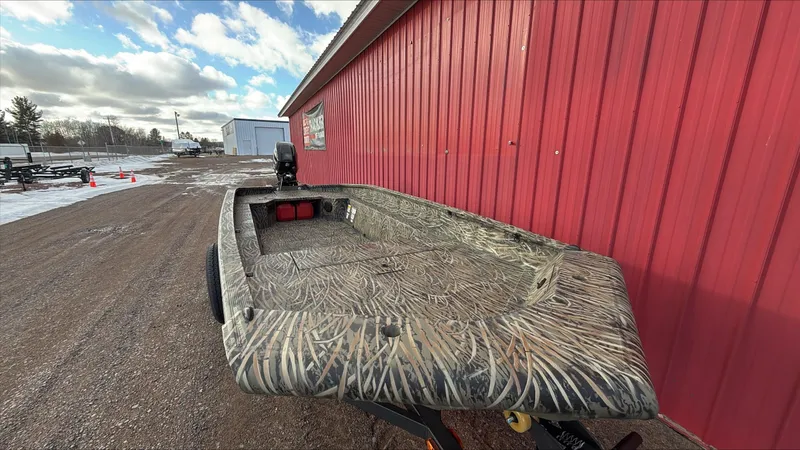 Slide: The Image of 2025 Tracker Grizzly 1650 T Prairie Wings Edition boat beside a red building. - 3