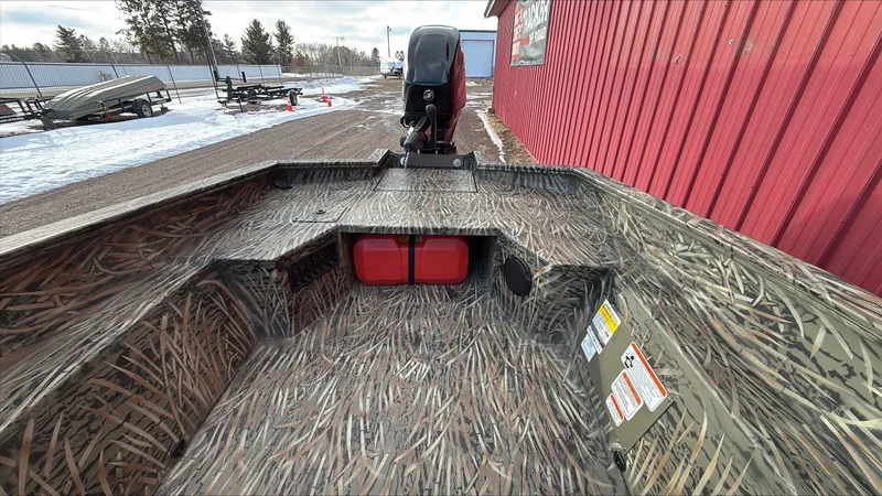 Slide: The Image of 2025 Tracker Grizzly 1650 T Prairie Wings Edition boat with camouflage design near red building. - 5