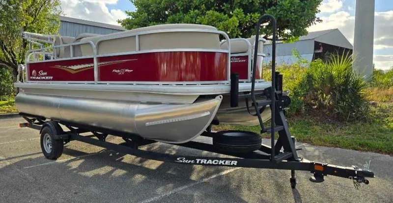 Slide: The Image of 2025 Sun Tracker Party Barge 18 DLX pontoon boat on trailer, parked outdoors. - 7