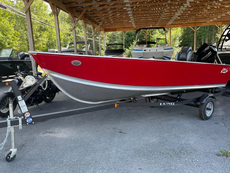 The Image of 2025 Lund 1600 Fury Tiller boat in red, parked on a trailer under a wooden shelter. - 0