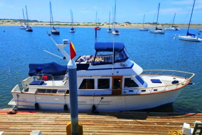 Slide: The Image of 1983 Ocean Alexander 43 yacht docked in a scenic marina with sailboats in the background. - 1