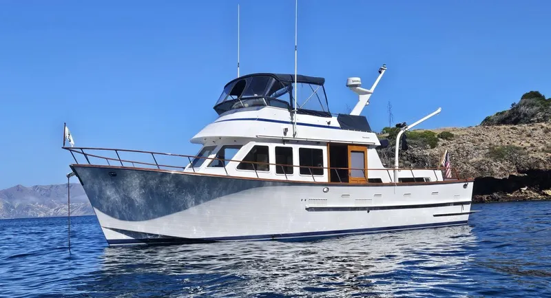 Slide: The Image of 1983 Ocean Alexander 43 yacht on calm blue water near rocky coastline. - 2