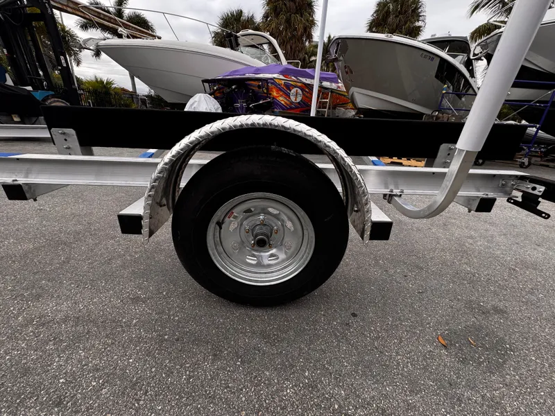 Slide: The Image of 2025 Single Axle Trailer with boats in background, parked on asphalt. - 11