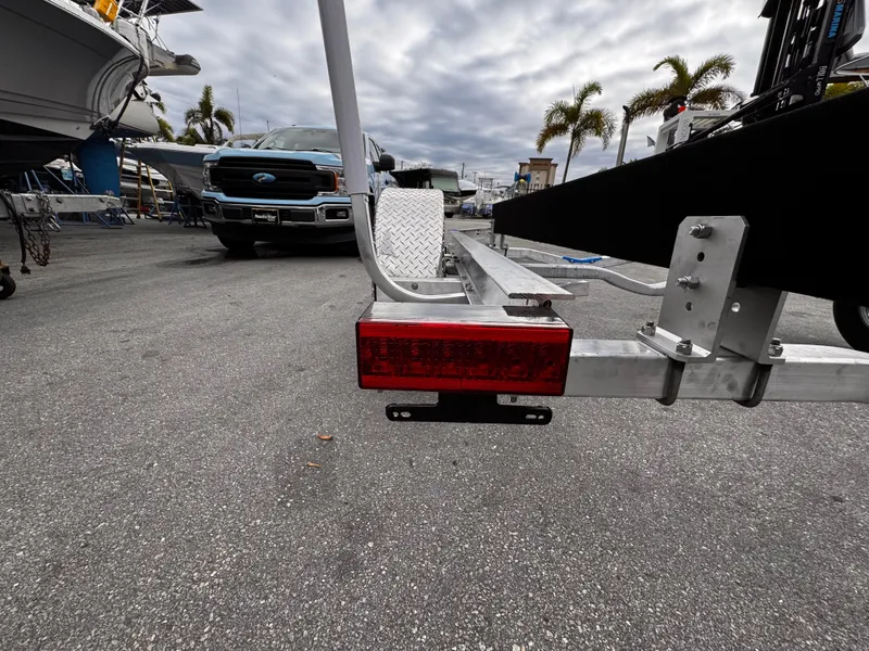Slide: The Image of 2025 Single Axle Trailer with red taillight, parked near trucks and palm trees. - 2
