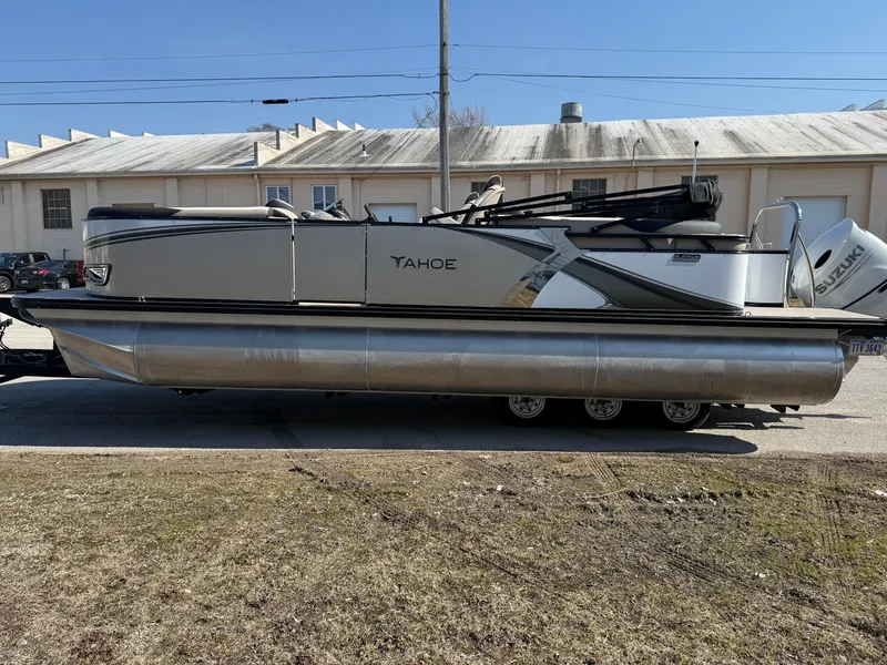 Slide: The Image of 2025 Tahoe Pontoon LTZ Quad Lounger on trailer, parked outdoors near industrial building. - 13