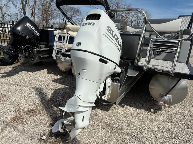 Slide: The Image of 2025 Tahoe Pontoon LTZ Quad Lounger with Suzuki outboard motor, parked on gravel. - 11