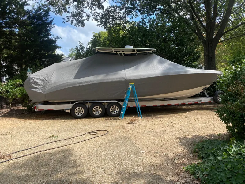 Slide: The Image of 2023 Statement 350 Open boat covered on trailer, parked outdoors with trees. - 30