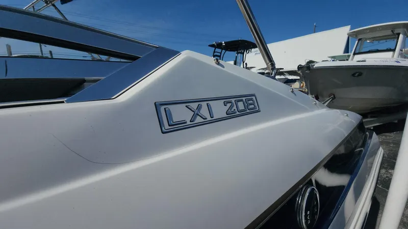 Slide: The Image of 2005 Larson LXi 208 boat, close-up of model name on hull, docked under clear blue sky. - 18