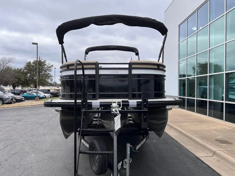 Slide: The Image of 2025 Harris Solstice 230 pontoon boat on trailer, parked near a glass building. - 11