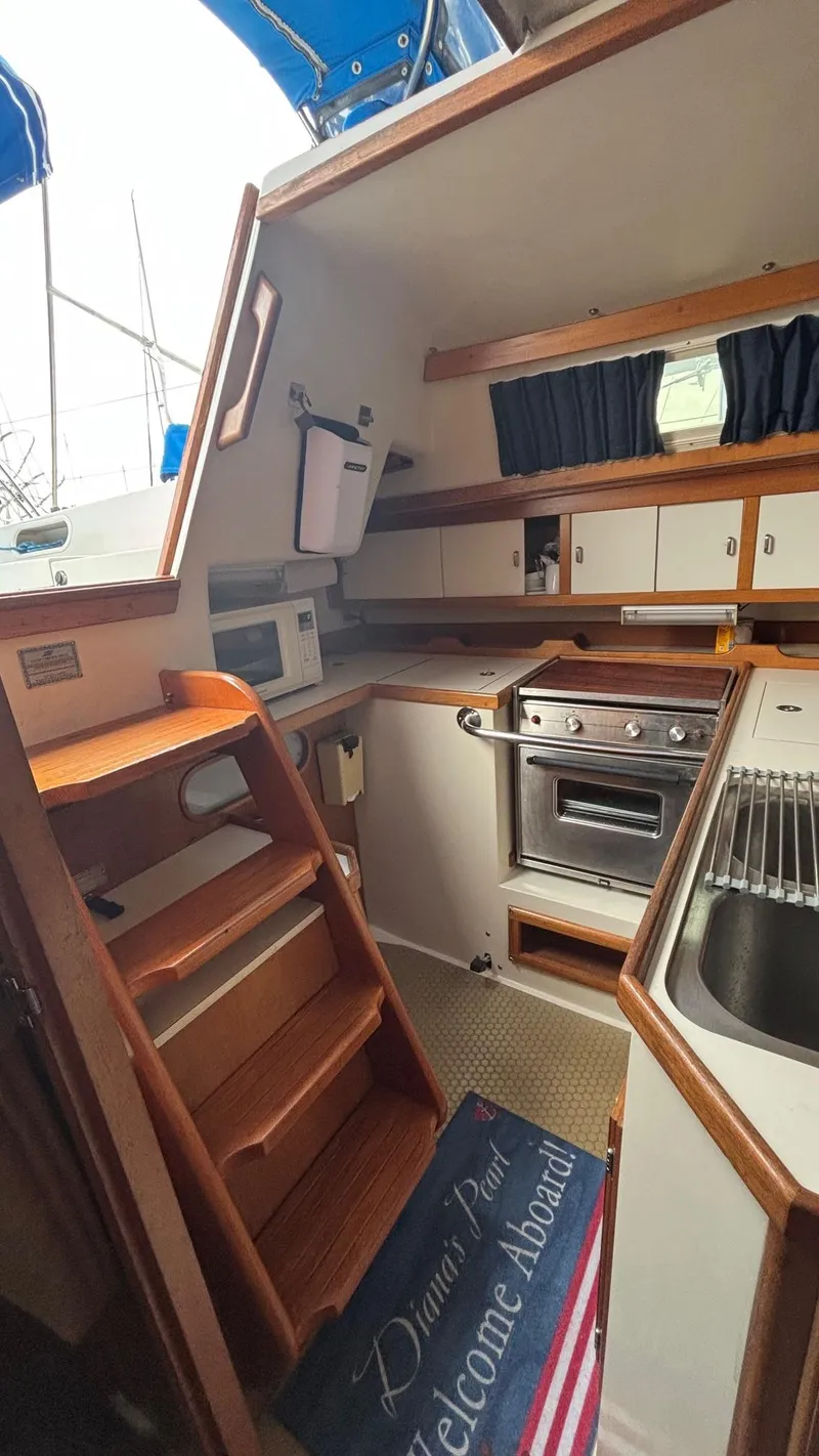 Slide: The Image of Interior of a 1994 Catalina 36 sailboat, featuring a compact kitchen with wooden cabinetry. - 28