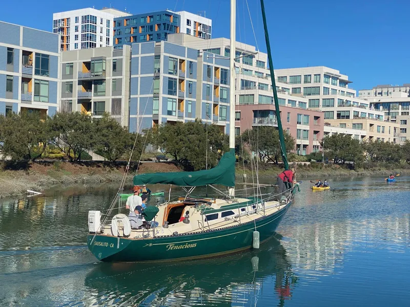 Slide: The Image of 1978 Islander sailboat cruising near modern waterfront buildings on a sunny day. - 2