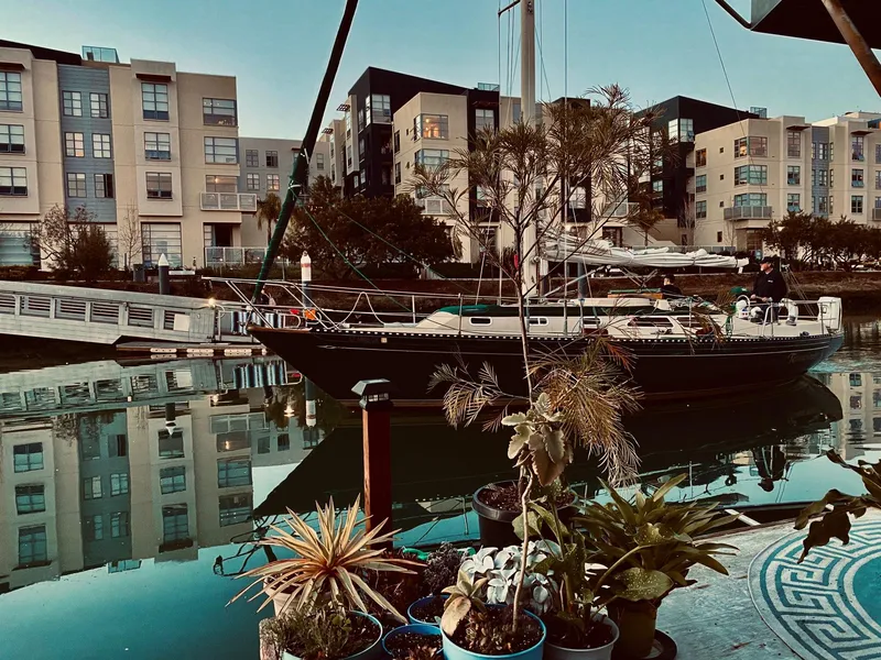 Slide: The Image of 1978 Islander sailboat docked in urban marina, surrounded by modern buildings and potted plants. - 3