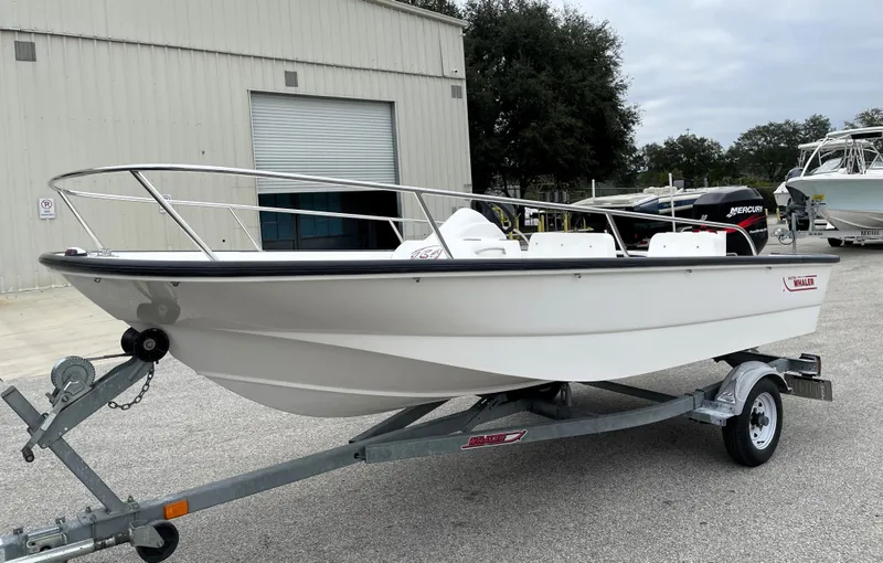 Slide: The Image of 2003 Boston Whaler 150 Sport boat on trailer, parked outdoors near a building. - 4