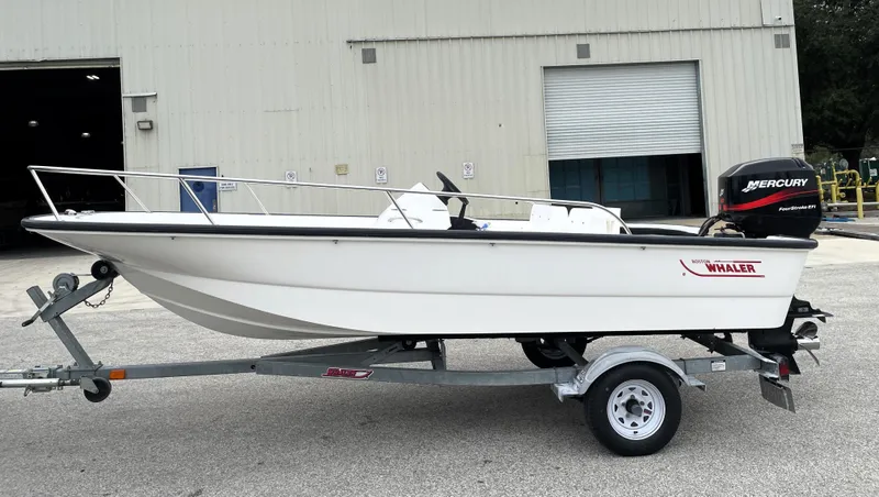 Slide: The Image of 2003 Boston Whaler 150 Sport boat on trailer, parked outside a warehouse. - 5