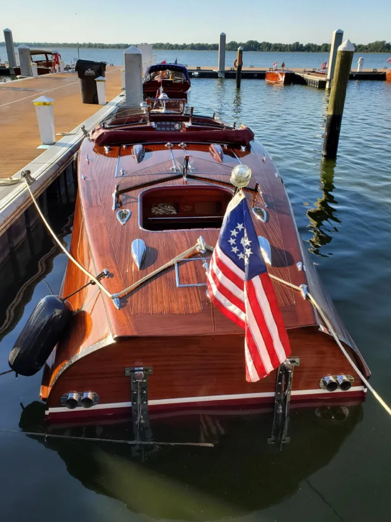 Slide: The Image of 2021 Classic Wilson Watercar docked, wooden finish, American flag, serene lake setting. - 12