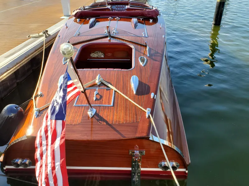 Slide: The Image of Classic 2021 Wilson Watercar with wooden finish docked by the water, featuring an American flag. - 13