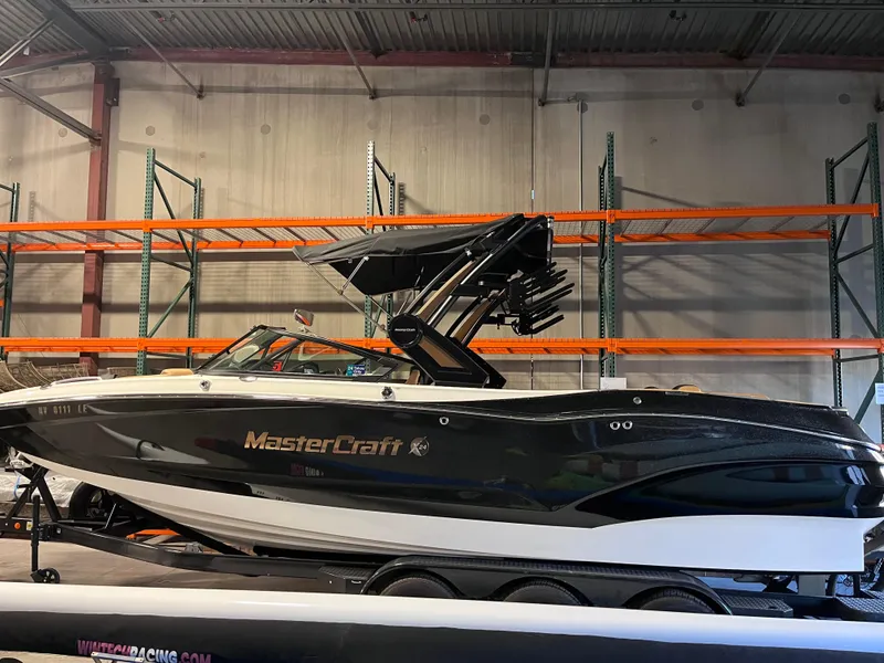 Slide: The Image of 2022 MasterCraft X24 boat in warehouse, black and white design, on trailer. - 0