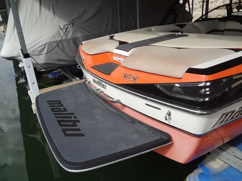 Slide: The Image of 2010 Malibu VLX Wakesetter boat with orange and white design, docked in a marina. - 7