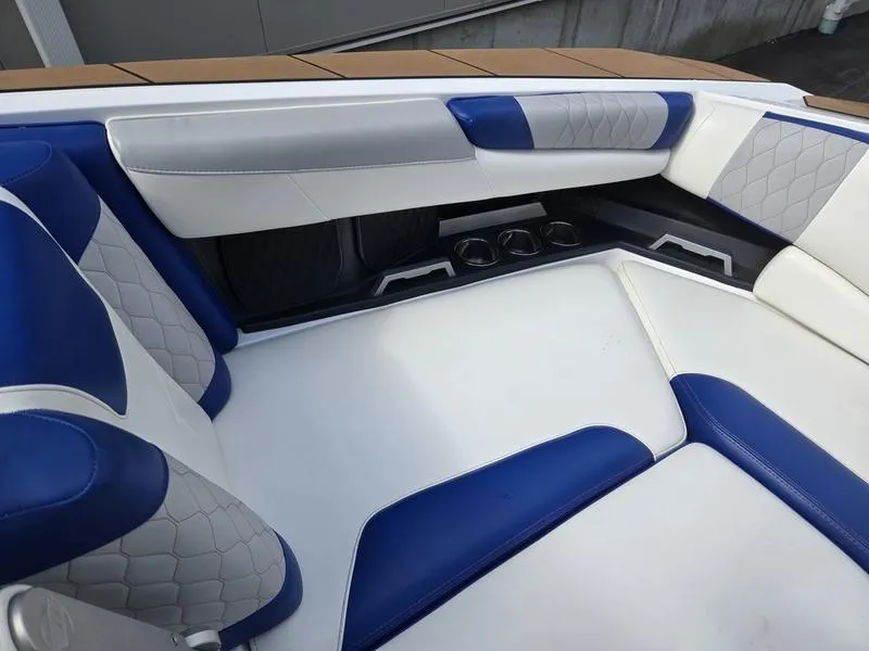 Slide: The Image of 2020 Malibu M240 boat interior with blue and white seating, featuring cup holders and quilted accents. - 29