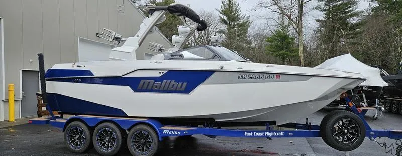Slide: The Image of 2020 Malibu M240 boat on trailer, white and blue design, parked outdoors. - 5