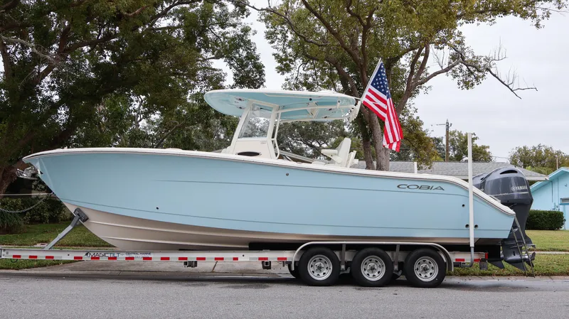 The Image of 2023 Cobia 280 Center Console boat on trailer with American flag. - 0