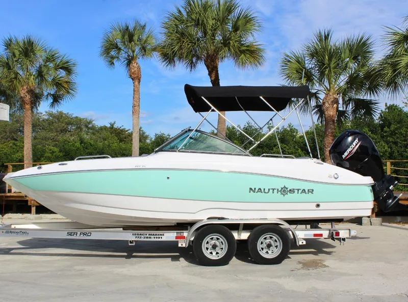 Slide: The Image of 2024 NauticStar DC Deck boat on trailer, palm trees in background. - 0