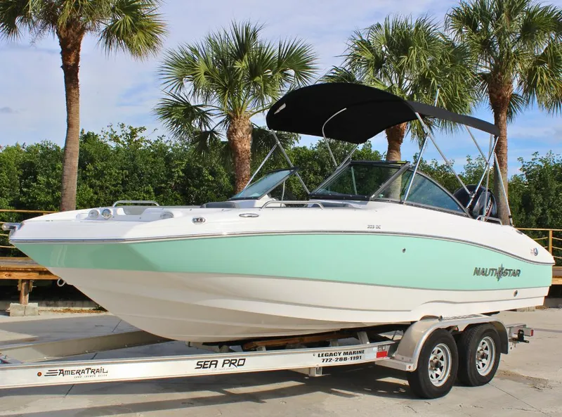 Slide: The Image of 2024 NauticStar DC Deck boat on trailer, parked near palm trees. - 1