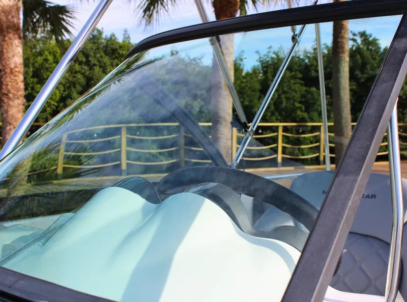 Slide: The Image of 2024 NauticStar DC Deck boat with windshield and steering wheel, surrounded by palm trees. - 26