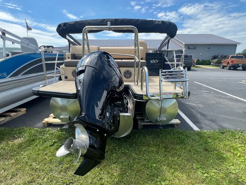 Slide: The Image of 2024 Harris Sunliner 230 pontoon boat with powerful outboard motor, parked on grass. - 6