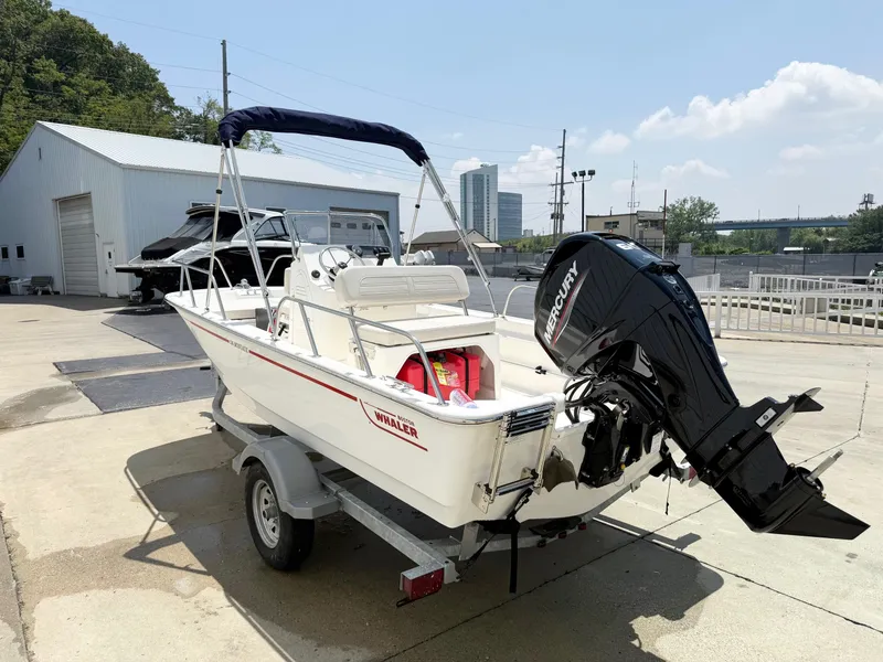 Slide: The Image of 2025 Boston Whaler 150 Montauk boat on trailer, parked outdoors, with Mercury outboard motor. - 3
