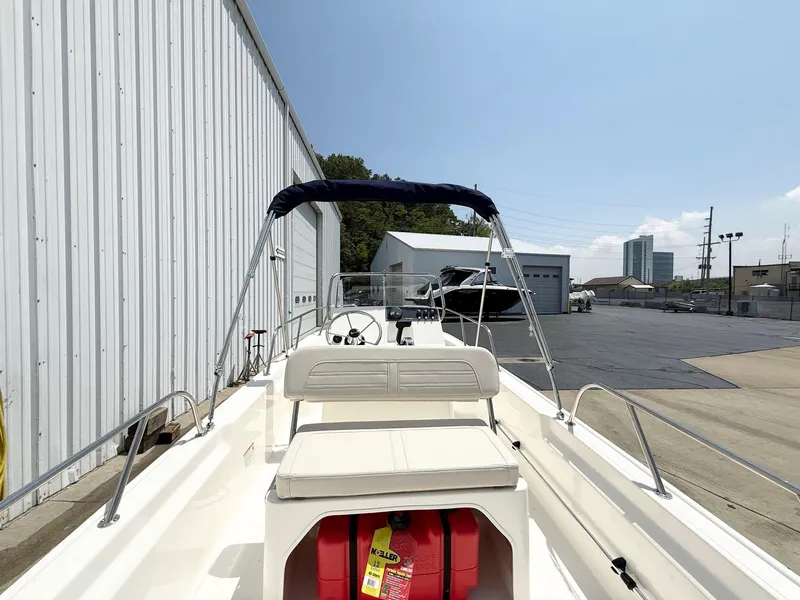Slide: The Image of 2025 Boston Whaler 150 Montauk boat with canopy, docked near industrial buildings. - 4