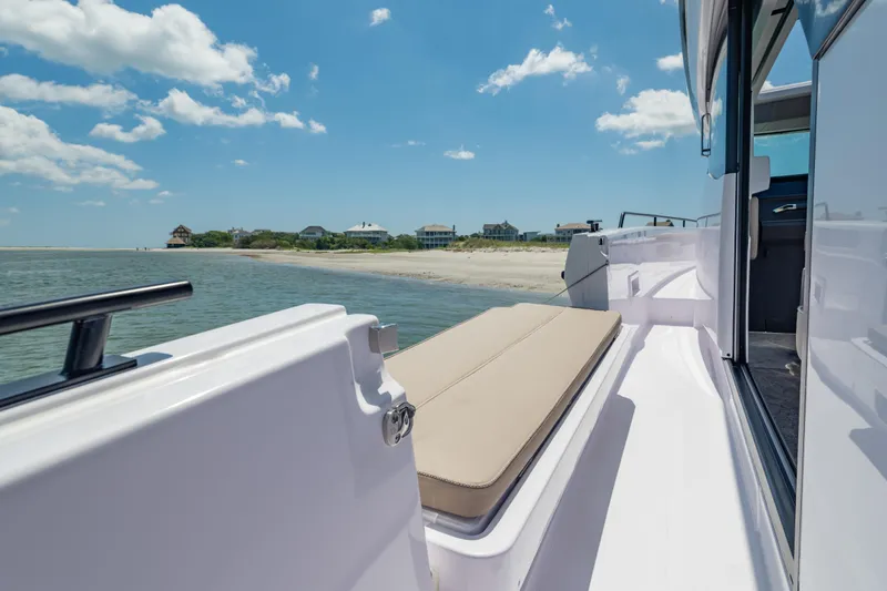 Slide: The Image of 2025 Axopar 45 XC Cross Cabin boat near a sandy beach under a clear blue sky. - 23