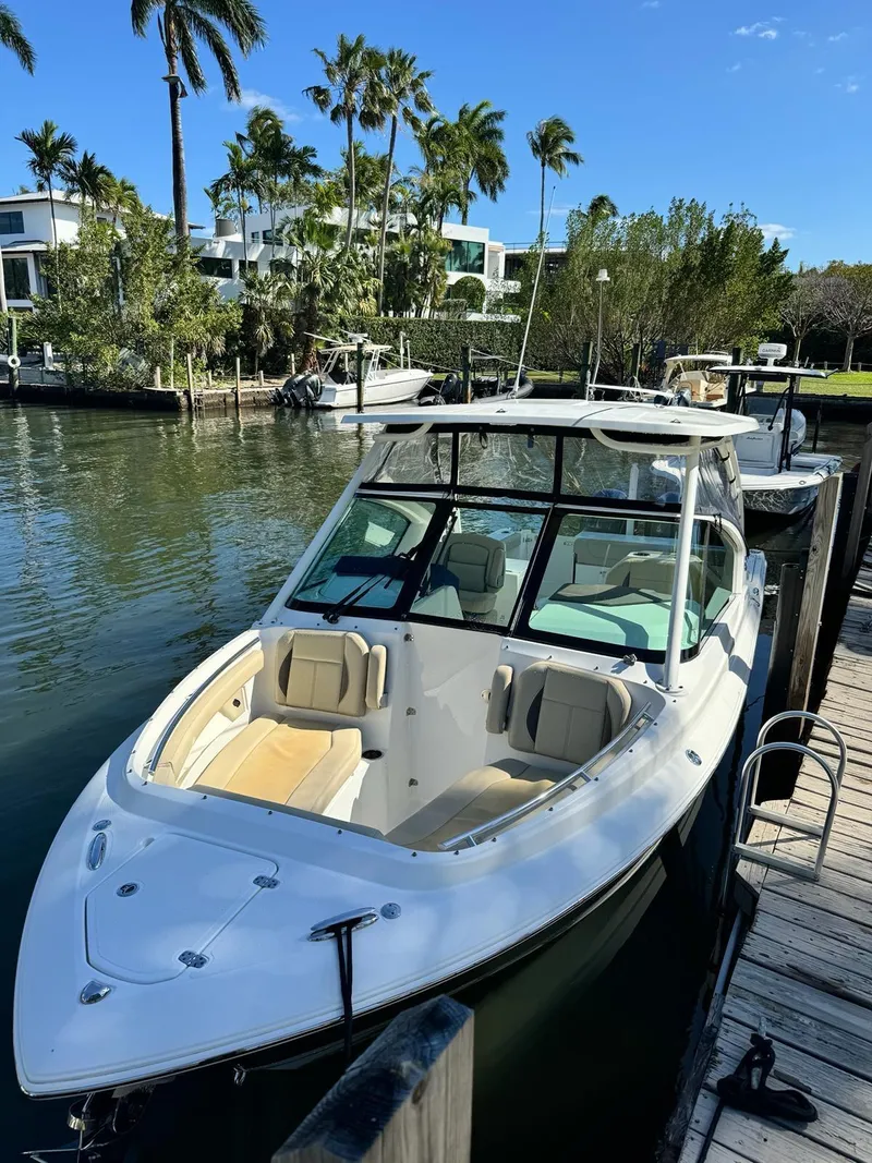 Slide: The Image of 2020 Pursuit 266 boat docked by palm trees and waterfront homes. - 2