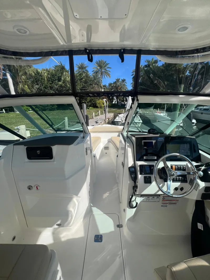 Slide: The Image of 2020 Pursuit 266 boat interior with steering wheel and dashboard, docked near palm trees. - 21