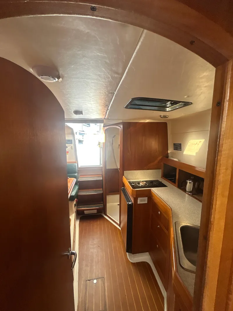 Slide: The Image of Interior of 2000 Mainship Pilot 34 boat, featuring wood cabinetry and compact kitchen area. - 16