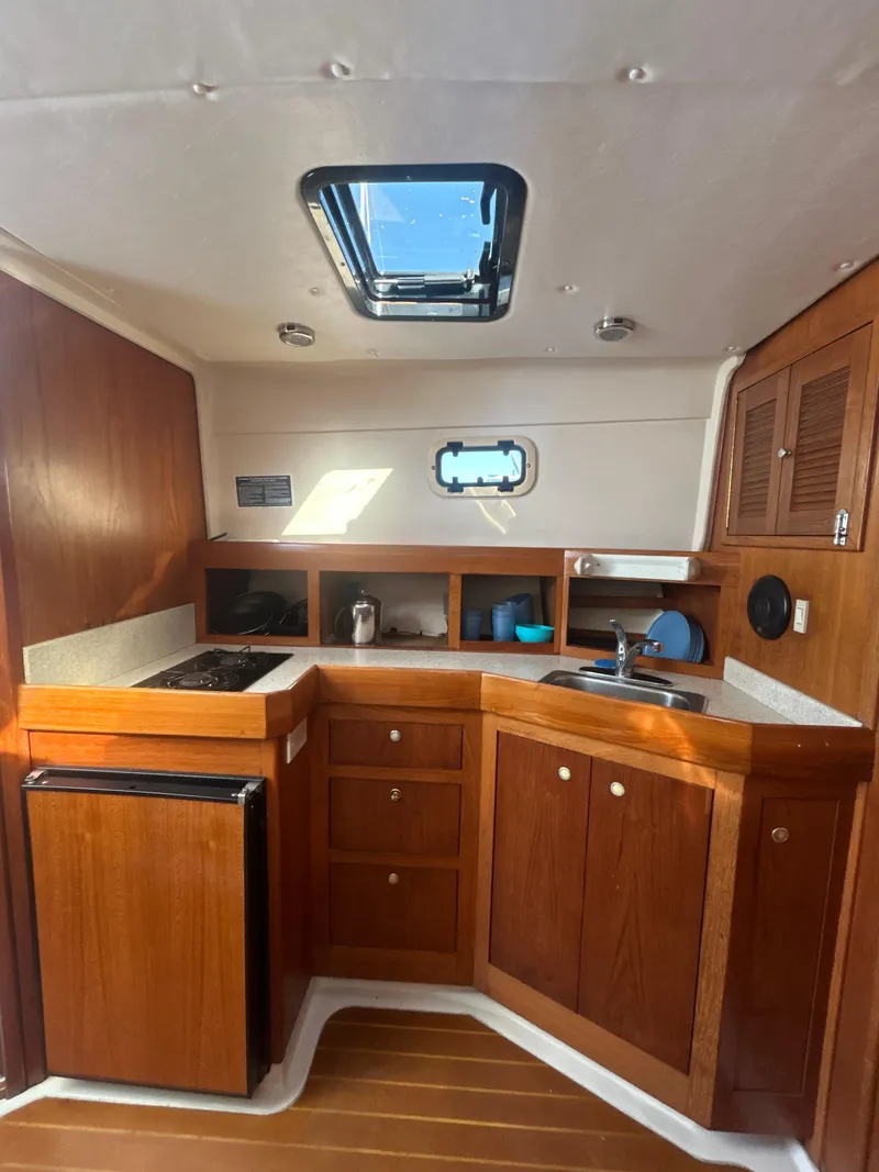 Slide: The Image of 2000 Mainship Pilot 34 boat interior with wooden cabinetry and compact kitchen area. - 20