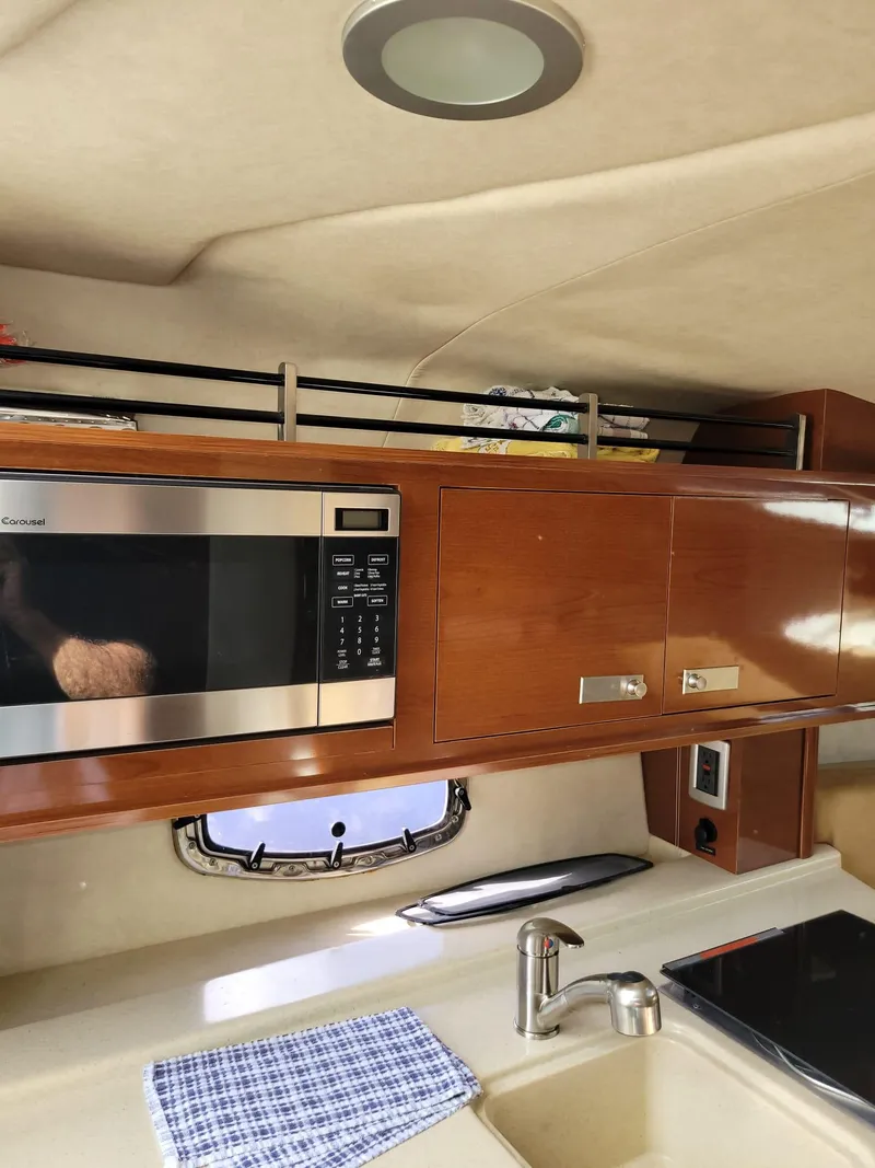 Slide: The Image of 2010 Sea Ray 280 Sundancer interior kitchen with microwave and wooden cabinets. - 23