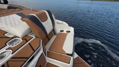 Slide: The Image of 2024 Malibu M242 boat interior with brown and white seating on a calm lake. - 9