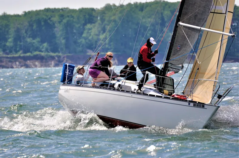 The Image of Sailboat Abbott 33 (1987) navigating choppy waters with crew, lush shoreline in background. - 0