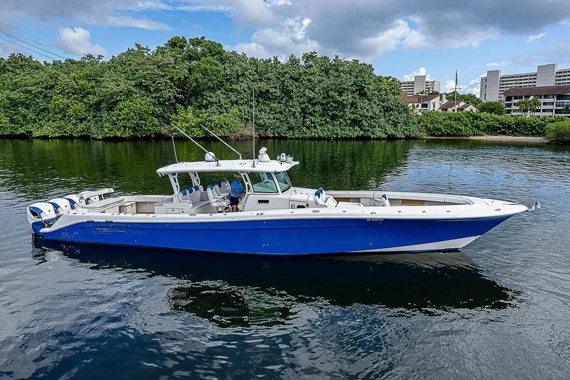 Slide: The Image of 2016 HCB 53 Sueños boat on calm water, surrounded by greenery and buildings. - 2